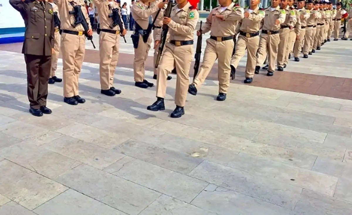 Cadets in beige uniforms marching in formation with rifles on a plaza