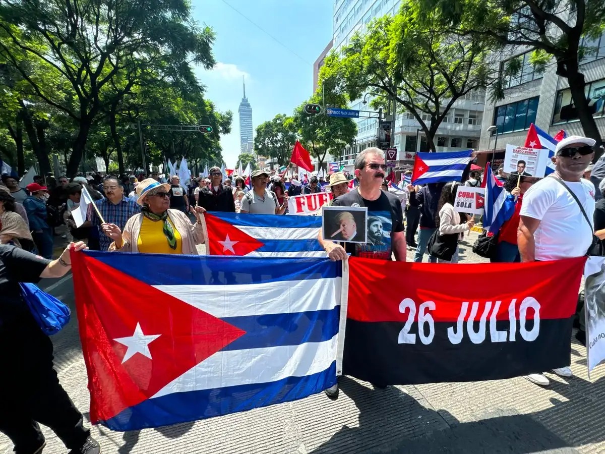 Marchers carry Cuban flags and a red-and-black July 26 Movement banner reading '26 Julio'