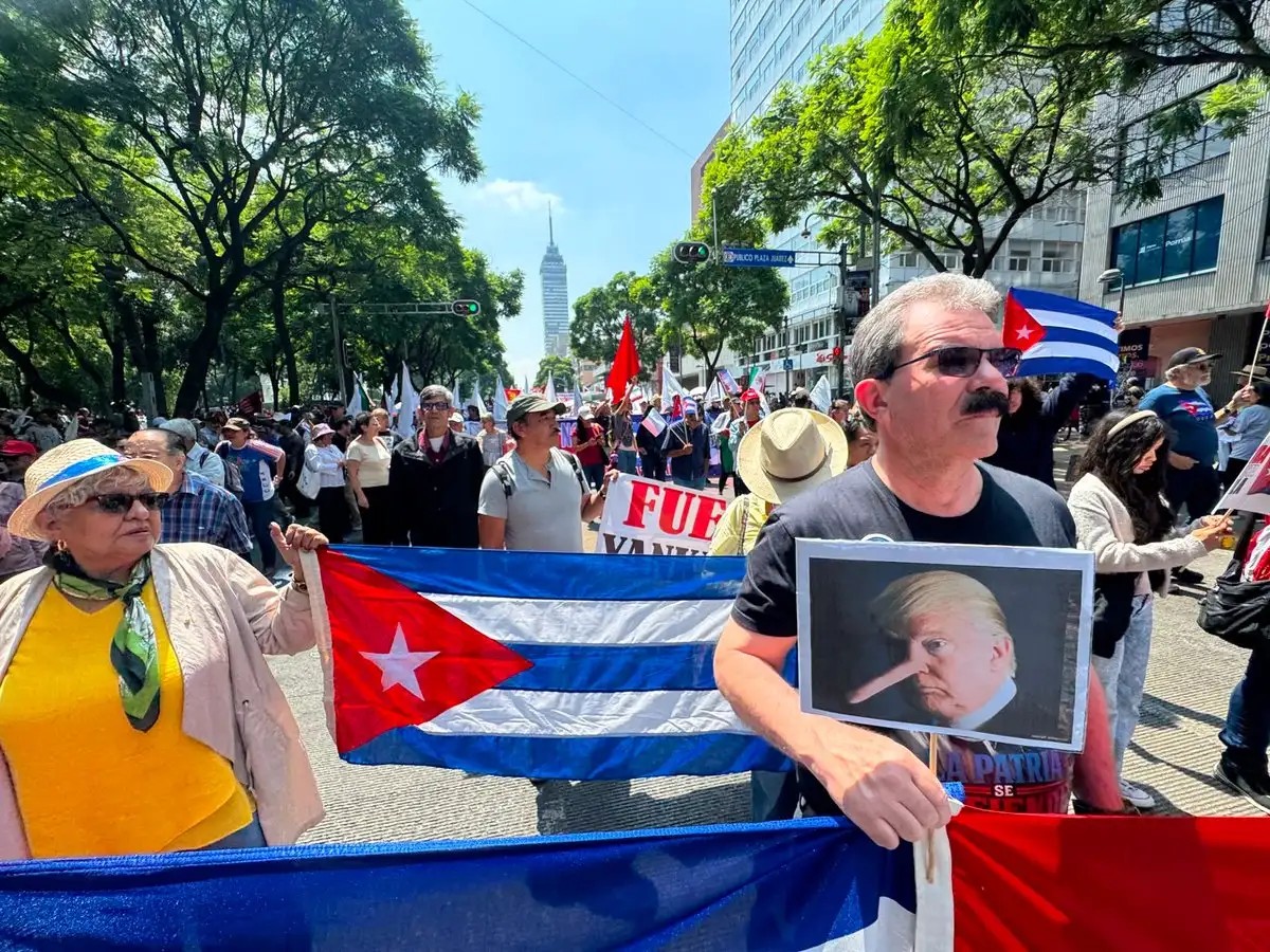 A demonstrator holds a placard depicting Donald Trump with a Pinocchio nose beside a Cuban flag