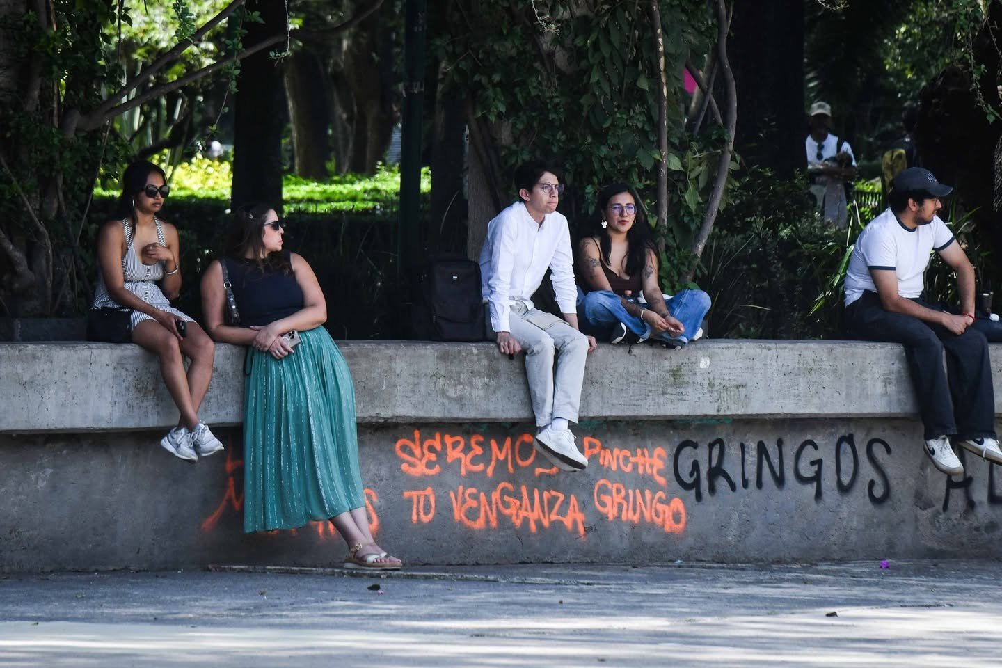 People sit on a wall covered with anti-gentrification graffiti in a Mexico City park