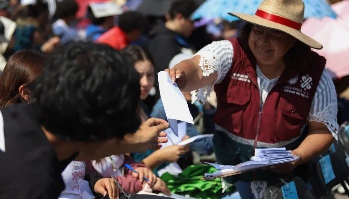 A government worker in a Secretariat of Well-Being vest hands out forms to a crowd