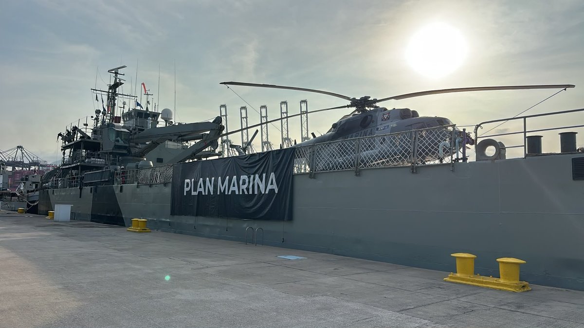 Navy ship with an MI-17 helicopter on deck and a Plan Marina banner