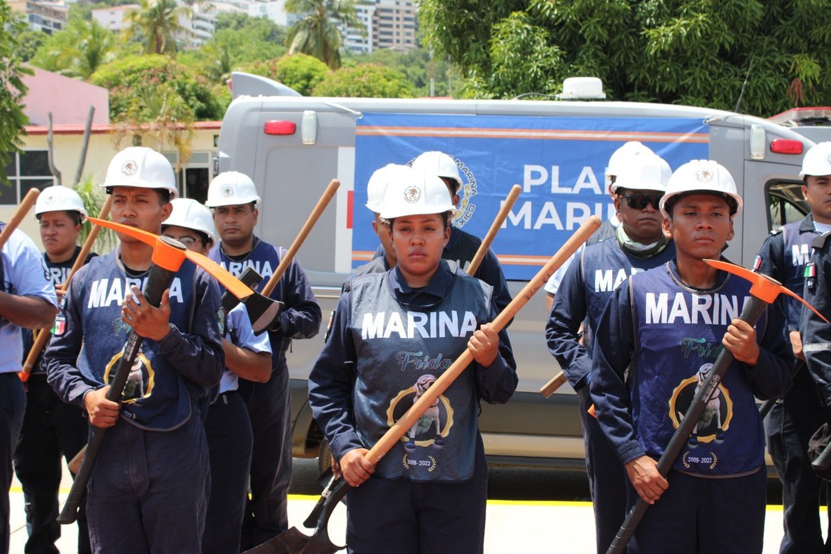 Navy personnel with shovels and picks in front of a Plan Marina vehicle