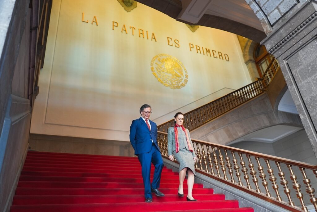 Gustavo Petro and Claudia Sheinbaum walk down the red-carpeted staircase of the National Palace beneath the inscription La Patria Es Primero.