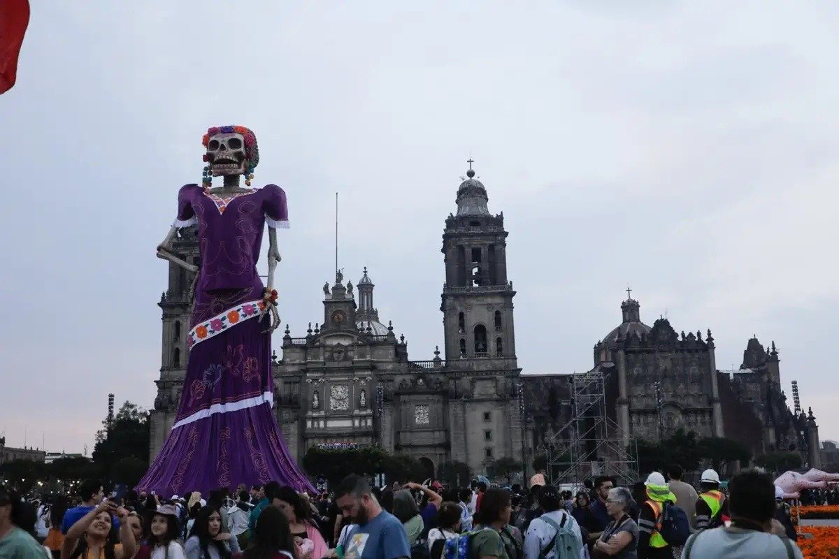 The giant catrina standing in front of the Metropolitan Cathedral as crowds gather in the Zócalo