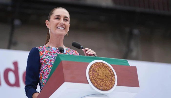 President Claudia Sheinbaum speaks from a podium bearing the Mexican coat of arms.