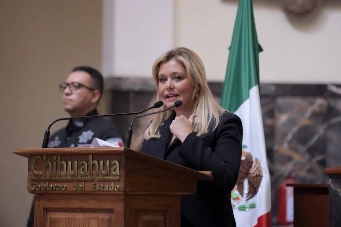 Maru Campos speaks at a Chihuahua state government podium beside a Mexican flag