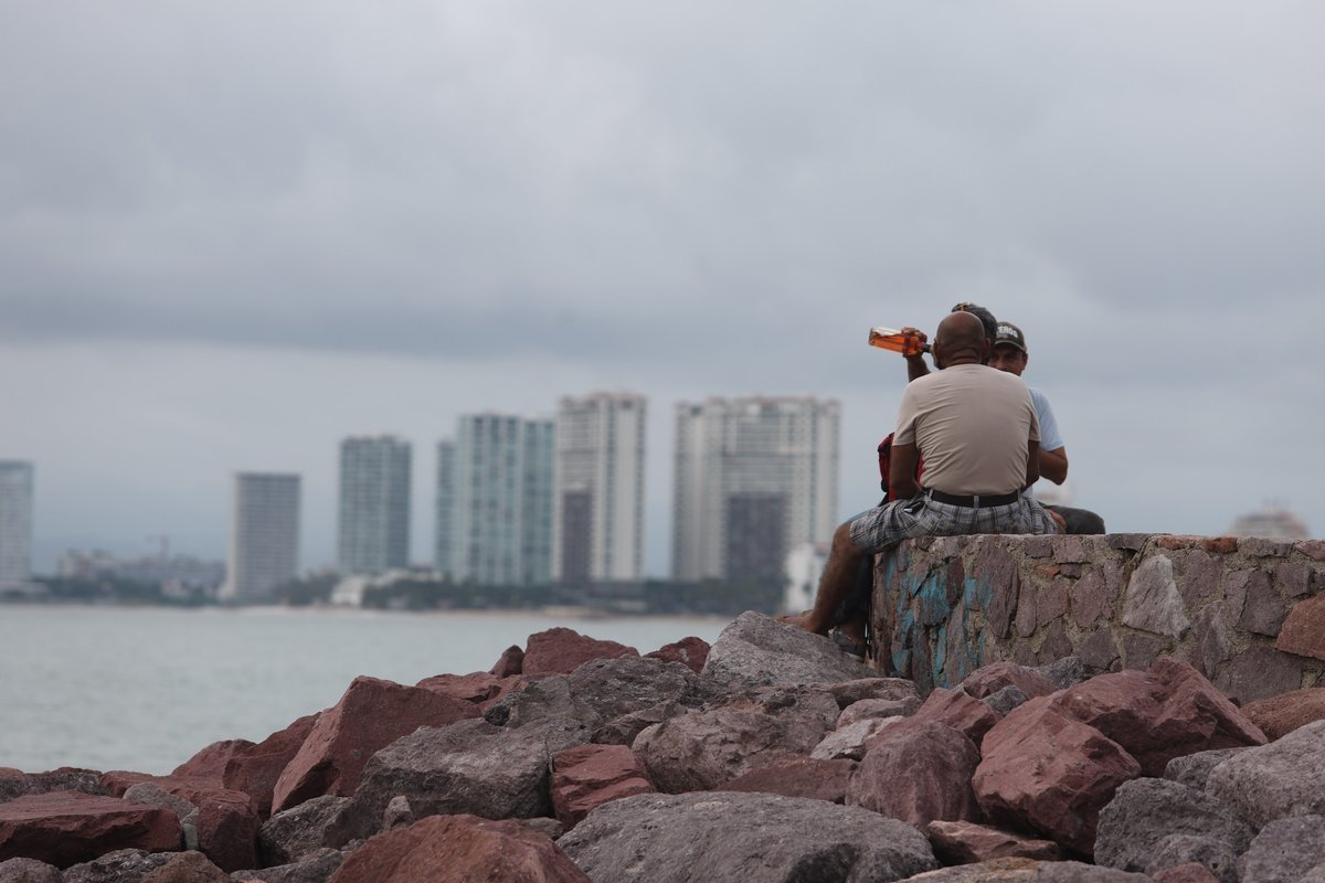 People sit on a seawall under cloudy skies on the Jalisco coast