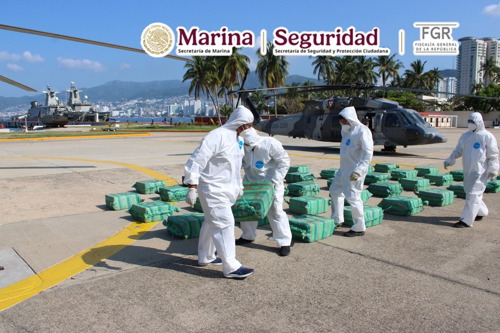 Navy personnel in protective suits unload packages of seized cocaine next to a helicopter