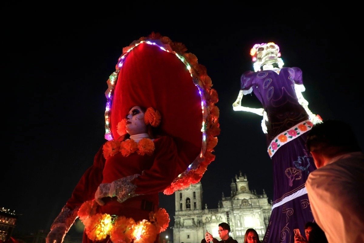 Illuminated catrina figures at night in the Zócalo, with the Metropolitan Cathedral behind